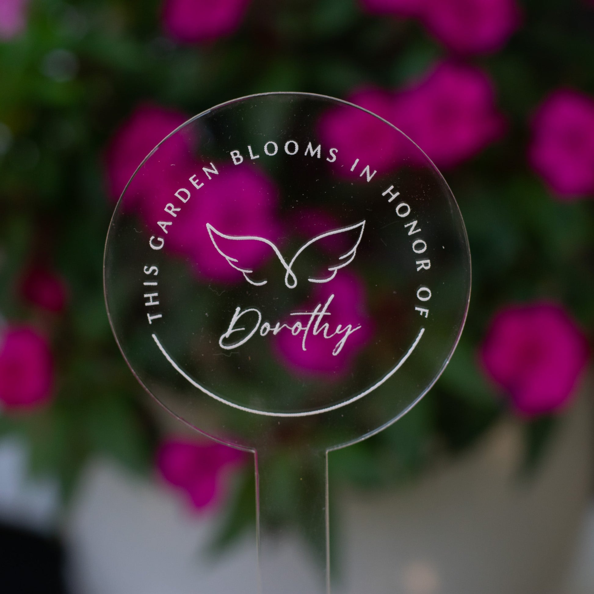 photo of a clear circular garden stake that displays angel wings and  "Dorothy" at the center and the words "This Garden Blooms In Honor Of" around the angel wings