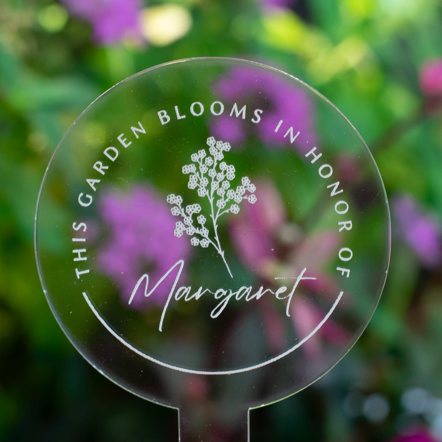 photo of a clear circular garden stake that displays a flower and  "Margaret" at the center and the words "This Garden Blooms In Honor Of" around the flower