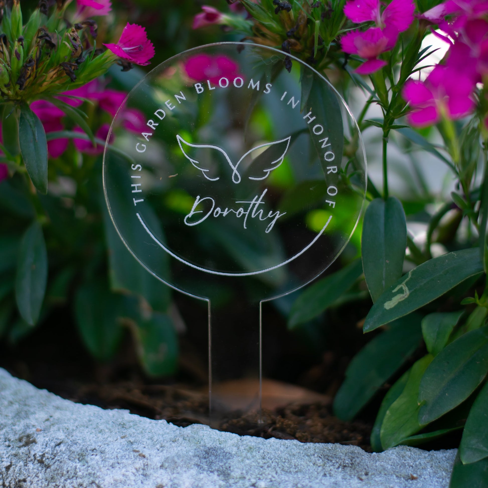 photo of a clear circular garden stake that displays angel wings and  "Dorothy" at the center and the words "This Garden Blooms In Honor Of" around the angel wings