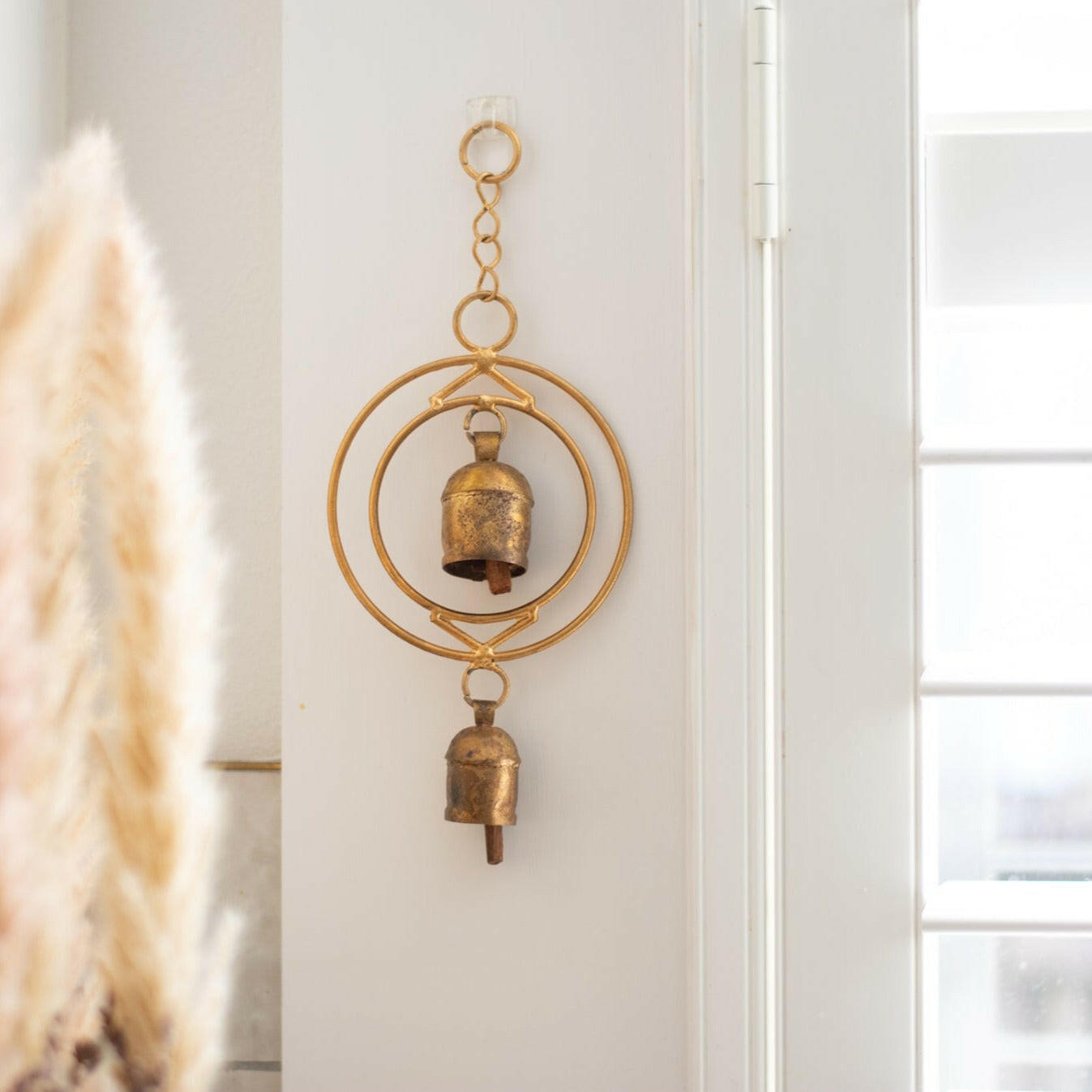 Close-up of a rustic wind chime of recycled tin and iron coated in copper with two bells hanging on a white post next to a white door